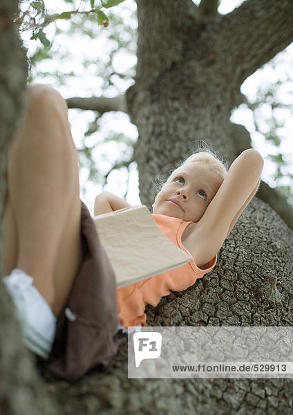 Mädchen im Baum liegend mit Buch auf dem Bauch