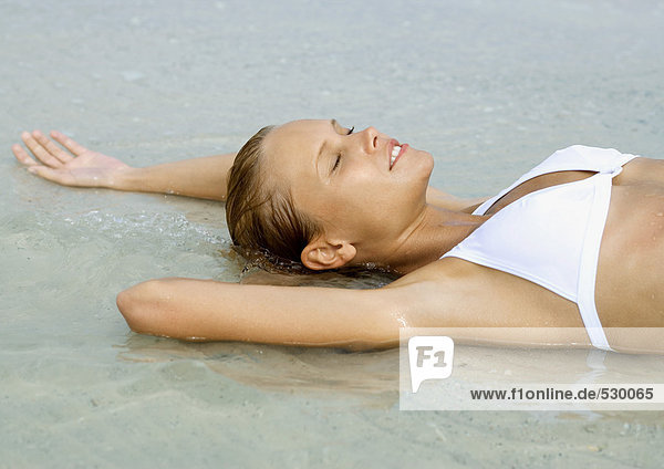 Frau im flachen Wasser am Strand liegend  Augen geschlossen