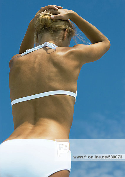 Frau in der Sonne stehend im Bikini  Hände hinter dem Kopf  niedriger Winkel  Rückansicht