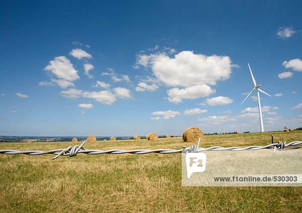 Windkraftanlage im Feld mit Heuballen  Stacheldraht im Vordergrund