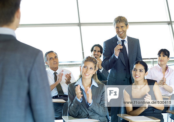 Executives in seminar  one man holding microphone  others clapping