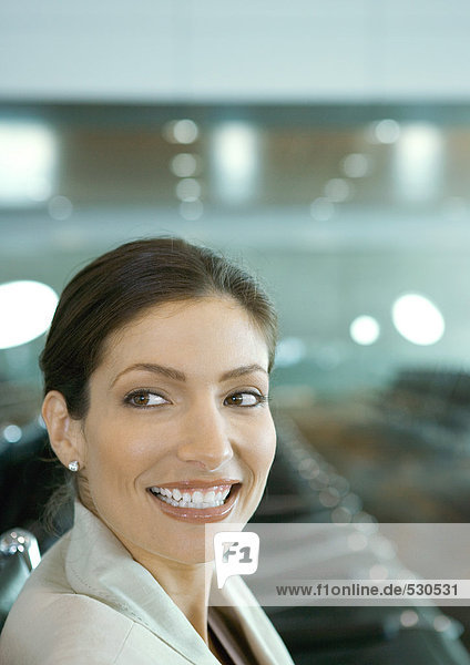 Frau in der Flughafenlounge  über die Schulter lächelnd