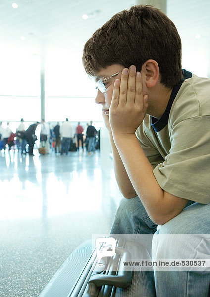 Junge sitzt am Flughafen und hält den Kopf.