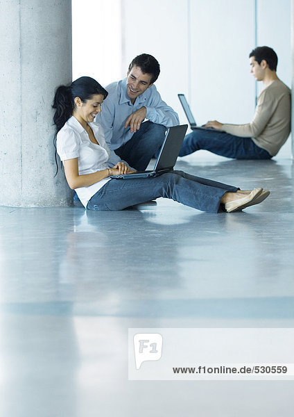 Mann und Frau auf dem Boden  mit Laptop und Sprechen  zweiter Mann im Hintergrund