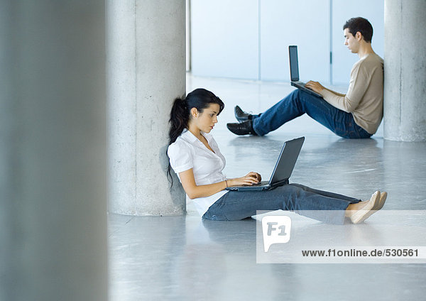 Young woman and young man sitting on floor  using laptops