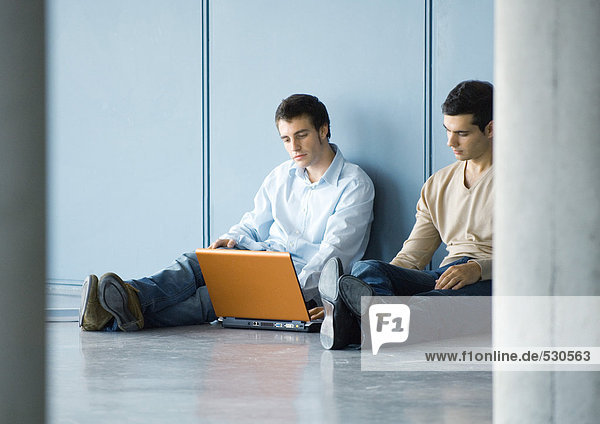 Zwei junge Geschäftsleute  auf dem Boden sitzend  mit Laptop