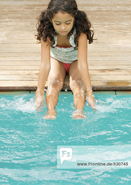 Girl sitting on edge of pool with hands and feet in water