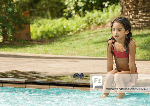 Girl sitting on edge of swimming pool with feet in water