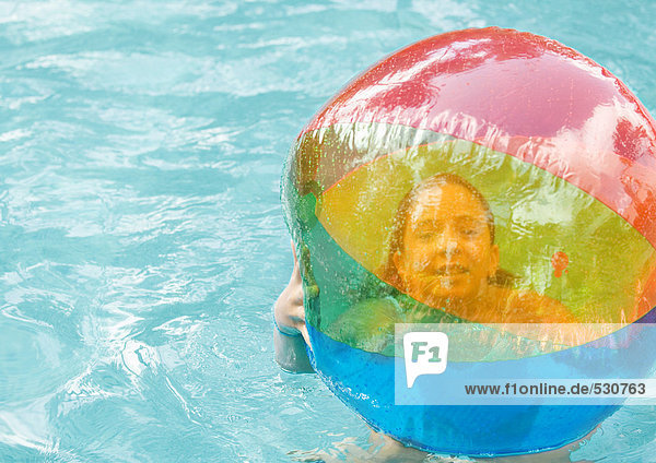 Little girl in swimming pool holding beach ball