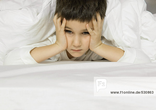 Child lying in bed  holding head