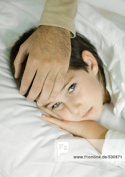 Kind im Bett liegend  Vaters Hand auf der Stirn