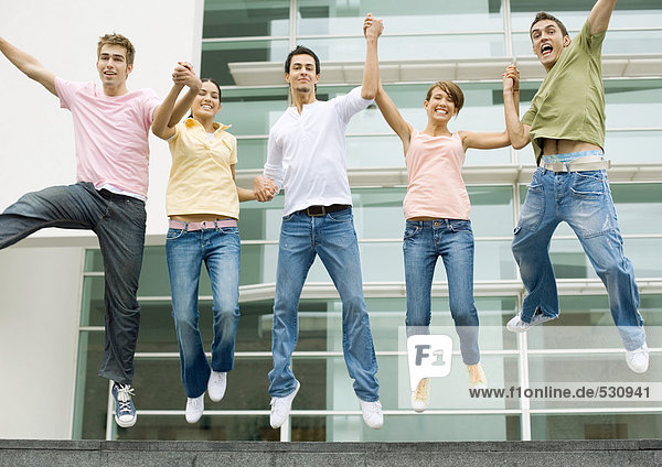 Teenager halten sich an den Händen und springen in der Luft.