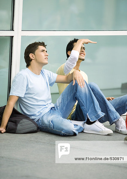 Jugendliche Männer sitzen auf dem Boden und schauen nach oben.