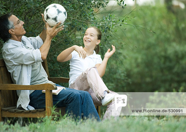Mädchen und Großvater sitzen zusammen und spielen mit dem Fußball.