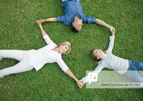 Erwachsenes Paar und Enkelin auf Gras liegend  Händchen haltend