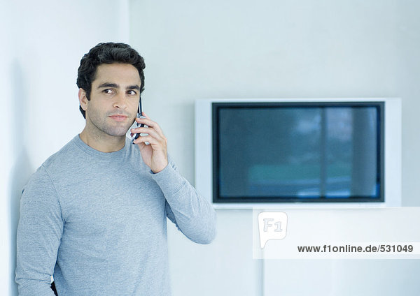 Mann mit Handy  Widescreen-TV im Hintergrund
