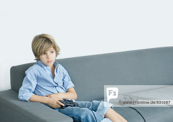 Junge sitzt auf dem Sofa und hält den Joystick.
