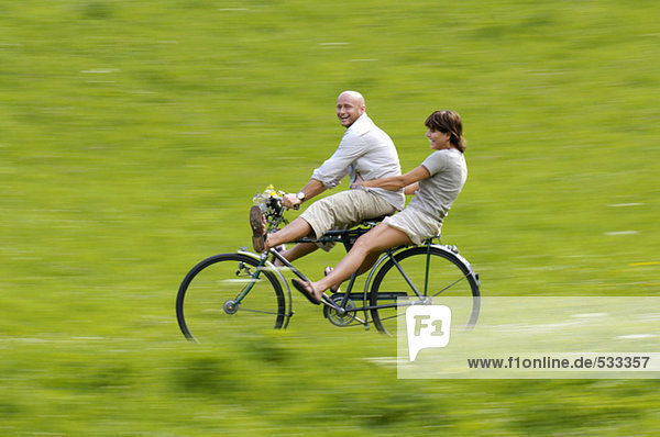 Couple riding bicycle in meadow  side view