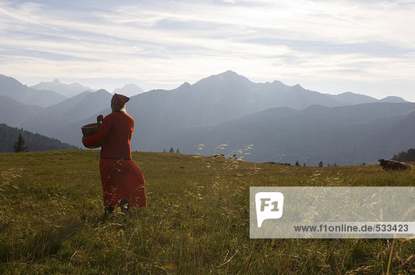 Peasant woman walking in meadow,  holding butter tub