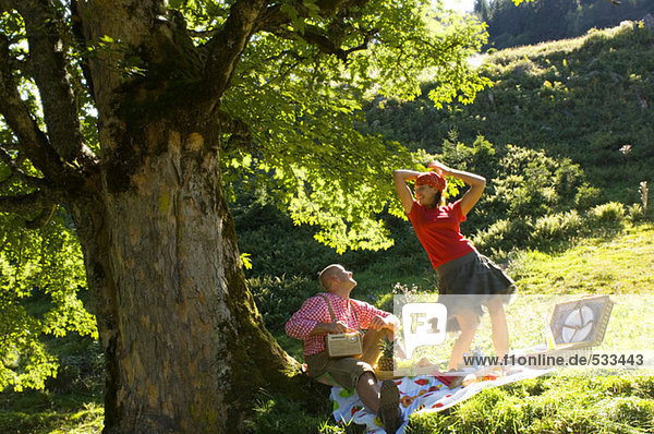 Pärchen beim Picknick unterm Baum,  Frau tanzt