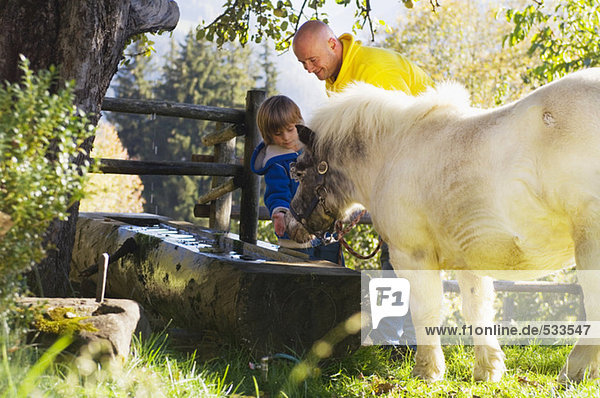 Vater und Sohn beobachten Pony am Brunnen