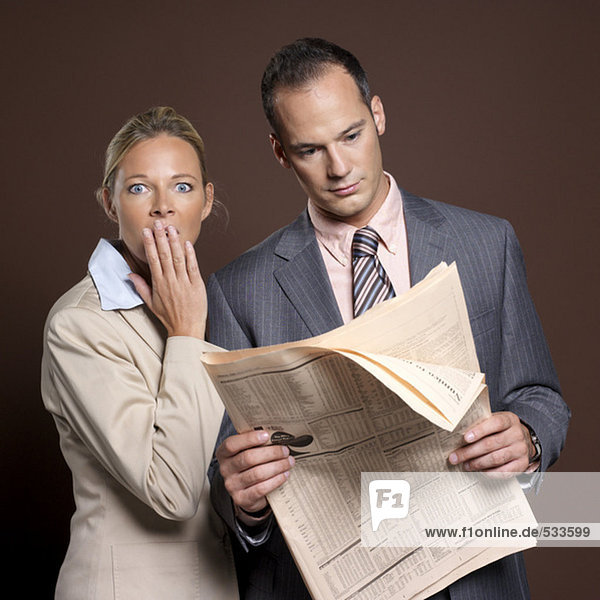 Businessman and businesswoman with newspaper,  woman covering mouth