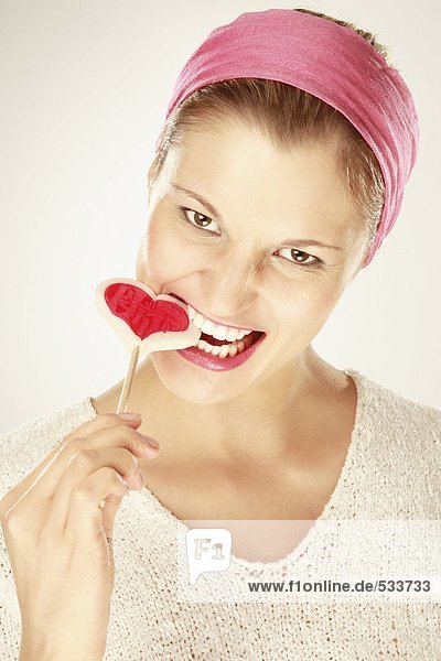 Junge Frau isst herzförmigen Lolli  Nahaufnahme  Portrait