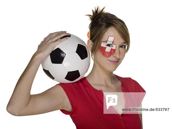 Junge Frau mit Schweizer Fahne auf dem Gesicht  hält Fußball auf der Schulter