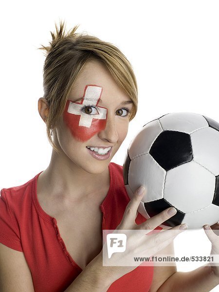 Junge Frau mit Schweizer Fahne auf Gesicht gemalt und Fußball haltend  Porträt