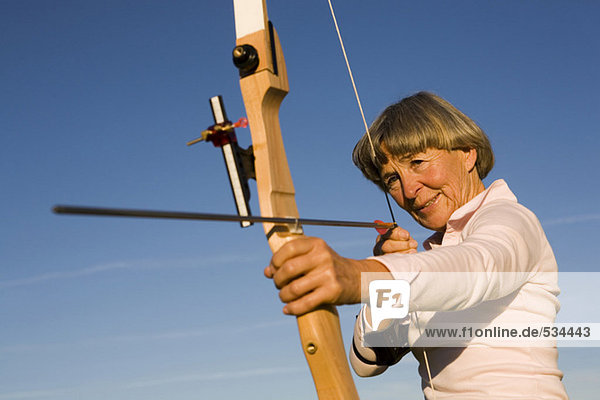Ältere erwachsene Frau mit Pfeil und Bogen