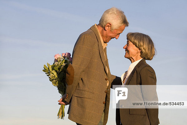 Seniorenpaar  Mann versteckt Blumenstrauß  lächelnd  Seitenansicht