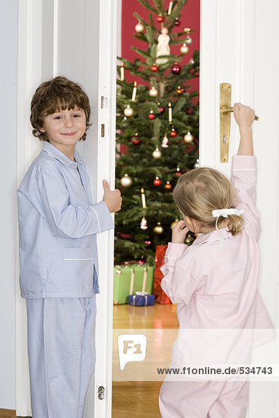 Mädchen und Junge stehen vor der Tür und beobachten den Weihnachtsbaum.