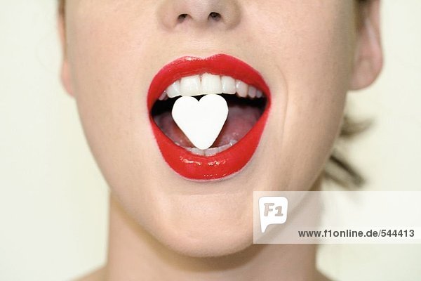 Close-up of woman eating heartshape candy mouth