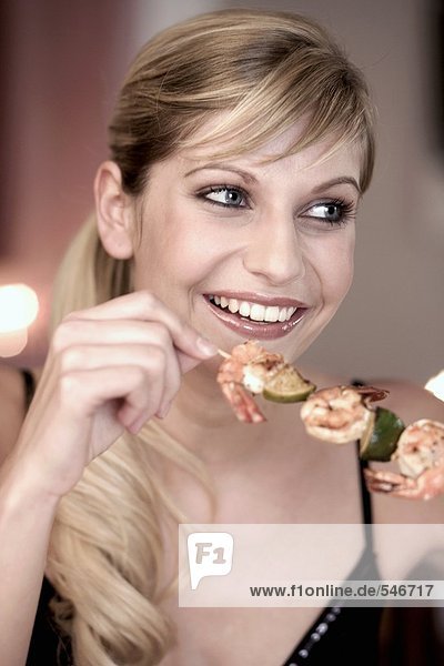 Junge Frau isst Garnelenspiess
