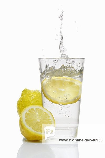 Eine Zitronensscheibe fällt in ein Glas Wasser
