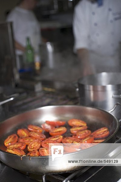 Tomaten in Bratpfanne auf dem Herd Köche im Hintergrund