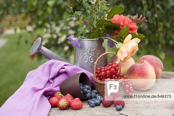 Pfirsiche  Beeren und Sommerblumen auf Tisch im Garten