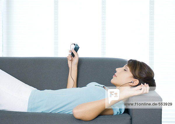 Junge Frau auf der Couch liegend  MP3-Player hörend
