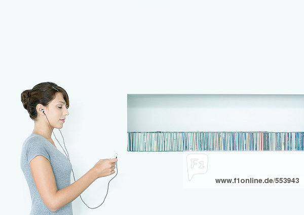 Junge Frau stehend  MP3-Player hörend  neben CD-Reihe  Augen geschlossen