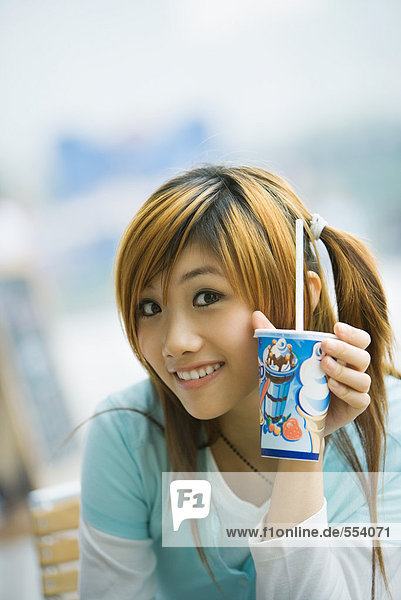 Junge Frau hält Fast-Food-Getränk hoch  lächelt in die Kamera