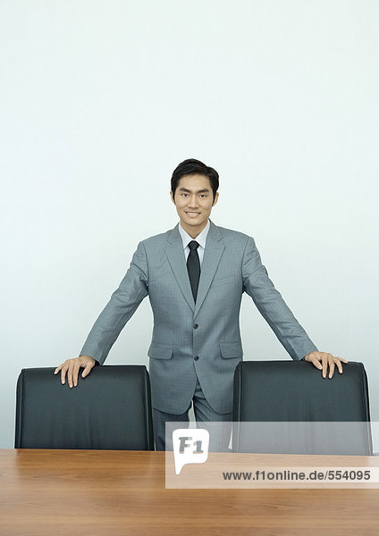 Geschäftsmann im Konferenzraum stehend mit den Händen auf Stuhllehnen  Portrait