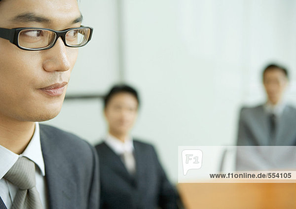Businessman glancing away  colleagues sitting in blurred background