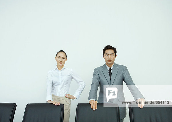 Männliche und weibliche Führungskräfte stehen mit den Händen auf Stuhllehnen  schauen in die Kamera  Porträt