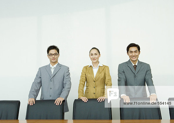 Geschäftsleute stehen mit den Händen auf Stuhllehnen im Konferenzraum