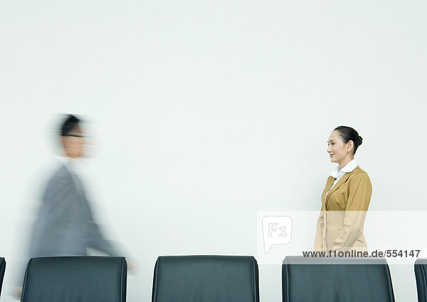Geschäftsfrau stehend  mit Blick auf die im Konferenzraum eintreffende Mitarbeiterin
