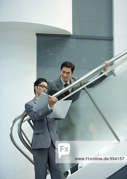 Geschäftsmann  der auf einer Treppe steht und auf die Akte seines Partners schaut.