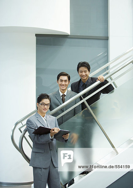 Drei Geschäftsleute  zwei stehen auf einer Treppe und lächeln in die Kamera.