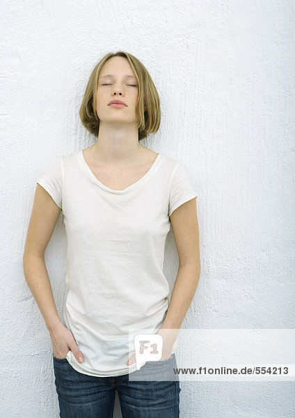 Teenage girl standing with hands in pockets  eyes closed  portrait
