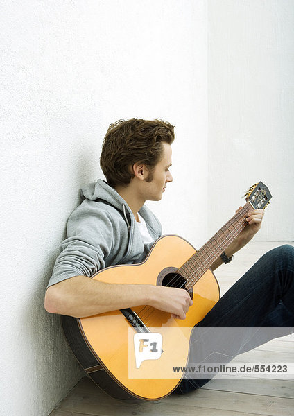 Young man sitting on floor  playing guitar