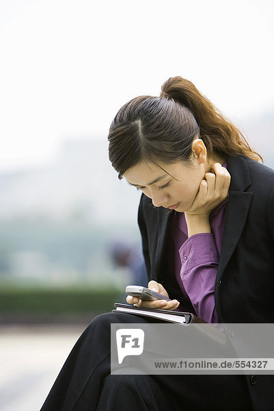 Geschäftsfrau mit Messaging-Telefon  nach vorne geneigt